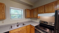 Located on Hancock Street in Marquette, Michigan, this single-floor unit offers a practical and well-organized layout suited for comfortable everyday living. The living area features warm hardwood flooring, a textured ceiling, and baseboard heating, with a entry door that brings in natural light and provides views of the lush greenery outside. The kitchen is equipped with warm oak cabinetry — both upper and lower — offering ample storage, complemented by gray laminate countertops, a double stainless steel sink, and a stainless steel electric range with an overhead exhaust hood. Tile flooring runs throughout the kitchen, and a window above the sink frames an inviting outdoor view. The bedrooms are carpeted for comfort, each featuring windows with blinds that allow natural light while maintaining privacy, along with closets and baseboard heating. The bathroom is clean and straightforward, outfitted with tile flooring, a full bathtub and shower combination, and standard fixtures. A dedicated laundry area with washer and dryer hookups adds convenience. Throughout the unit, neutral wall tones and consistent wood-accented details create a cohesive, understated aesthetic well-suited to the Marquette, MI setting.