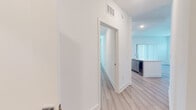 This well-appointed single-floor residence showcases a clean, contemporary design characterized by crisp white walls, light wood-tone luxury vinyl plank flooring, and recessed lighting throughout. The open-concept kitchen serves as a central highlight, featuring floor-to-ceiling gray shaker cabinetry, a white quartz peninsula with an undermount sink, a white subway tile backsplash, and a full suite of stainless steel appliances including a range, over-the-range microwave, and French door refrigerator. The living area is bright and airy, benefiting from natural light delivered through multiple windows with horizontal blinds and a sliding glass door fitted with vertical blinds that opens to an outdoor view. The bedrooms are generously proportioned, each with neutral walls, light flooring, and windows that bring in natural light. Two bathrooms serve the unit: a full bath with a soaking tub and tiled shower surround paired with a gray vanity, and a second bathroom featuring an elongated vanity with white countertops, a framed mirror, and a glass-enclosed shower. A dedicated laundry room houses a full-size, top-loading washer and dryer with built-in shelving above, adding exceptional in-unit convenience. The overall ambiance is modern, bright, and move-in ready.