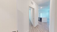 This well-appointed single-floor residence showcases a clean, contemporary design characterized by crisp white walls, light wood-tone luxury vinyl plank flooring, and recessed lighting throughout. The open-concept kitchen serves as a central highlight, featuring floor-to-ceiling gray shaker cabinetry, a white quartz peninsula with an undermount sink, a white subway tile backsplash, and a full suite of stainless steel appliances including a range, over-the-range microwave, and French door refrigerator. The living area is bright and airy, benefiting from natural light delivered through multiple windows with horizontal blinds and a sliding glass door fitted with vertical blinds that opens to an outdoor view. The bedrooms are generously proportioned, each with neutral walls, light flooring, and windows that bring in natural light. Two bathrooms serve the unit: a full bath with a soaking tub and tiled shower surround paired with a gray vanity, and a second bathroom featuring an elongated vanity with white countertops, a framed mirror, and a glass-enclosed shower. A dedicated laundry room houses a full-size, top-loading washer and dryer with built-in shelving above, adding exceptional in-unit convenience. The overall ambiance is modern, bright, and move-in ready.