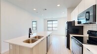 Located at 630 E Main Ave in Bismarck, North Dakota, this modern one-bedroom, one-bathroom unit offers a thoughtfully designed open-concept layout that maximizes every square foot. Light wood-tone flooring runs throughout, creating a warm and cohesive aesthetic across all rooms.

The kitchen is a standout feature, anchored by a generous peninsula with a crisp white quartz countertop and a double stainless steel sink with a matte black faucet. White upper cabinetry with a subway tile backsplash pairs cleanly with light wood lower cabinets, while black appliances — including a refrigerator, range, and microwave — provide a bold contrast. Recessed lighting illuminates the space efficiently.

The bedroom is bright and airy, featuring a large black-framed window that floods the room with natural light and frames views of the surrounding Bismarck cityscape. The clean white walls amplify the sunlight, creating a welcoming and restful atmosphere. A dedicated closet provides practical storage.

The bathroom is clean and functional, finished with light wood-tone flooring consistent with the rest of the unit. It includes a vanity with storage, a full bathtub, and a well-placed mirror. Black hardware accents tie the design together cohesively throughout the space.