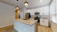 Located at 4604 Hammersley Rd in Madison, Wisconsin, this single-floor unit offers a thoughtfully designed, modern living space with a clean, contemporary aesthetic. The open-concept layout centers around a well-appointed kitchen featuring a large granite-topped island with an undermount sink, crisp white shaker-style cabinetry with matte black hardware, and a full suite of stainless steel appliances including a refrigerator, electric range, and built-in microwave. Stylish pendant lighting above the island adds a warm, inviting focal point to the space. Light hardwood-style flooring flows seamlessly throughout the main living areas, enhancing the bright and airy feel of the interior. The living area is spacious and open, with sliding glass doors that lead to a private outdoor balcony, allowing for natural light and exterior views. The bedroom features plush carpeting, a ceiling fan, and a window that brings in additional natural light. The bathroom is finished with a granite-topped vanity with gray cabinetry and modern fixtures, maintaining the consistent upscale detailing found throughout the unit. Neutral wall tones and clean white trim contribute to a cohesive, move-in-ready atmosphere that balances modern finishes with everyday functionality.