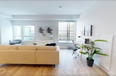 This contemporary 74 square meter apartment offers a perfect blend of style and functionality. The open-concept design maximizes the use of space, featuring two living room areas that flow seamlessly into each other. The kitchen is a standout, boasting sleek wooden cabinetry, stainless steel appliances, and a convenient breakfast nook with modern seating.

The bedroom, spanning 10 square meters, is a serene retreat with large windows that flood the space with natural light. It's adorned with a comfortable bed, minimalist decor, and a striking circular wall art piece that adds visual interest.

The bathroom is a study in modern design, featuring clean white tiles, a combination tub and shower, and contemporary fixtures. The use of a gray shower curtain adds a touch of sophistication to the space.

Throughout the apartment, hardwood flooring lends warmth and continuity. The living areas are thoughtfully furnished with a mix of contemporary pieces, including a comfortable yellow sofa, sleek coffee tables, and strategically placed artwork that enhances the overall aesthetic.

Large windows in the living areas not only provide ample natural light but also offer views of the surrounding area, creating a sense of openness and connection to the outdoors. The apartment's design emphasizes a neutral color palette with occasional pops of color, resulting in a space that feels both fresh and inviting.