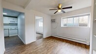 This efficient 2-bedroom, 1-bathroom unit is thoughtfully laid out across a single floor, offering a practical and functional living space. The main living area features wood-look flooring, a ceiling fan with light fixture, a wall-mounted air conditioning unit, and a baseboard heating system. Large windows allow natural light to filter in, providing views of the surrounding greenery. A built-in shelving unit adds additional storage to the living space.

The kitchen is outfitted with white cabinetry, granite-patterned countertops, and white appliances including a coil-burner range, over-the-range microwave, and a full-size refrigerator. The wood-look flooring continues seamlessly throughout, and ample cabinet and counter space makes the kitchen both organized and functional.

The primary bedroom features a ceiling fan, a built-in closet with sliding doors, and a window overlooking the outdoors. The second bedroom is carpeted, with a baseboard heater and a window providing natural light. Both rooms offer a quiet, comfortable atmosphere.

The bathroom is finished with marble-style large-format wall tiles surrounding a soaking bathtub, complemented by beige floor tiles and brushed nickel fixtures. The clean, white vanity and crisp finishes create a polished look throughout.