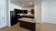 Located at 1202 W 200 N, Unit 205 in Centerville, UT, this 780-square-foot, single-floor apartment offers 2 bedrooms and 2 bathrooms with a functional and modern layout. The open living area features light-toned luxury vinyl plank flooring, a ceiling fan, and a glass door with an adjacent window that fills the space with natural light and provides outdoor views. The kitchen is a standout feature, equipped with dark espresso cabinetry, granite countertops, black appliances including a refrigerator, electric range, and over-the-range microwave, along with a central granite-topped island perfect for additional prep space or casual dining. Both bathrooms are finished with dark vanity cabinetry, granite countertops, large mirrors with overhead lighting, and LVP flooring. The two bedrooms are carpeted and bright, with the primary bedroom measuring 160 square feet and featuring a window with natural light. A dedicated closet provides additional storage. The unit's neutral white walls and consistent finishes throughout create a clean, cohesive aesthetic well-suited for comfortable everyday living.