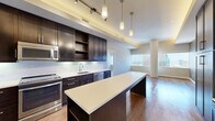 Located at 350 N Saint Paul St in the heart of downtown Dallas, TX, this well-appointed one-bedroom residence offers a refined urban living experience with sweeping skyline views. The open-concept layout makes excellent use of its space, flowing seamlessly between rooms with warm hardwood flooring and clean architectural lines.

The kitchen is a standout feature, designed with dark espresso cabinetry, stainless steel appliances, and a generous central island topped with a light countertop surface. Ambient cove lighting along the tray ceiling adds a warm glow, while pendant lights over the island and track lighting provide functional illumination. Ample cabinet storage and open shelving complete this well-equipped culinary space.

The living area is bathed in natural light through large floor-to-ceiling windows that frame dramatic views of the Dallas skyline. A distinctive architectural column adds character to this bright, airy space, which features warm hardwood flooring and a tray ceiling with cove lighting.

The spacious primary bedroom is generously proportioned, featuring plush carpeting, elevated ceilings with a ceiling fan, and access to an en-suite bathroom. Large windows continue the skyline views, creating a bright and serene retreat. A dedicated closet provides organized storage. The overall ambiance is modern, sophisticated, and ideally suited for urban living in one of Dallas's most prominent locations.