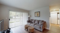 Located at 14200 SW Teal Blvd in Beaverton, Oregon, this single-floor residence offers a well-organized layout designed for comfortable everyday living. The living room serves as the heart of the space, featuring light wood-style flooring, soft neutral walls, and abundant natural light streaming through large vertical-blind-covered sliding glass doors that open to an outdoor patio area with surrounding greenery. A secondary window further brightens the room, enhancing its open and airy feel.

Adjacent to the living area is a dedicated dining space, finished with the same wood-style flooring and accented by a ceiling fan with integrated lighting. A window with horizontal blinds allows natural light into the area, while the entry door is conveniently positioned nearby.

The kitchen is thoughtfully designed with white shaker-style cabinetry, dark countertops, and a full suite of stainless steel appliances, including a refrigerator, electric range, microwave, and dishwasher. A peninsula provides additional prep space and visual separation from the adjacent hallway, which leads to in-unit laundry facilities.

The bedroom offers a comfortable, carpeted retreat, while the bathroom is clean and functional, featuring a full soaking tub and shower combination with chrome fixtures and a curtain rod. The overall ambiance throughout is bright, neutral, and move-in ready.