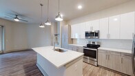 This single-story, 2-bedroom, 2-bathroom residence in Memphis, Tennessee offers a well-appointed, modern interior with a cohesive design aesthetic throughout. The open-concept kitchen serves as the centerpiece of the living area, featuring a large center island with a white quartz countertop, an undermount sink, and stylish brushed nickel pendant lighting overhead. Cabinetry combines crisp white upper cabinets with warm wood-toned lower cabinets, complemented by a herringbone-patterned tile backsplash. Stainless steel appliances, including a range, microwave, refrigerator with ice maker, and dishwasher, complete the kitchen. Wood-look flooring extends seamlessly through the kitchen, living, and dining areas, adding warmth and continuity. The living area is spacious and open, with access to a private outdoor area through glass doors. Both bedrooms are well-sized, featuring wood-look flooring, neutral walls, ceiling fans, and natural light from windows. The two bathrooms are finished with granite countertops, wood-toned vanity cabinets, and framed mirrors. One bathroom includes a soaking tub with white subway tile surround and brushed nickel fixtures, maintaining the clean, contemporary style found throughout the residence.