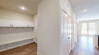 Located in Grapevine, TX, this single-story home offers a thoughtfully designed floor plan with three bedrooms, two bathrooms, and a seamless blend of functional and modern finishes throughout. The kitchen is a standout feature, boasting white upper cabinetry with glass-front accents, gray lower cabinetry, granite countertops, subway tile backsplash, stainless steel appliances, and a large center island with a deep single-basin sink illuminated by elegant gold pendant lights. Light wood-style flooring flows through the main living areas, creating a warm and cohesive aesthetic. The generously sized primary bedroom features large sliding glass doors that allow abundant natural light to fill the space, complemented by a ceiling fan. A well-appointed walk-in closet with built-in shelving and dual hanging rods serves the primary suite. The primary bathroom includes a glass-enclosed walk-in shower with white tile surround and brushed gold fixtures, alongside a soaking tub with a granite ledge. Secondary bedrooms feature plush carpeting, ceiling fans, and large windows. A dedicated mudroom with white shaker-style upper cabinets, built-in bench, and cubbies adds everyday convenience. The attached garage provides additional storage and parking space, rounding out this well-equipped home.