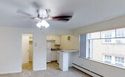 Located at 1001 Sherman Street in Denver, Colorado, this single-floor residence offers a straightforward and functional layout well-suited for comfortable everyday living. The main living area is carpeted and bright, featuring a ceiling fan with integrated lighting that helps maintain airflow and ambiance throughout the space. Neutral white walls keep the interior feeling clean and open.

The kitchen is positioned at the edge of the living area and is equipped with white cabinetry, a white range and refrigerator, and a countertop that extends to form a convenient breakfast bar or pass-through surface. The kitchen flooring transitions to tile, providing a practical surface for the cooking and prep area. A baseboard heater is also visible near the window, ensuring warmth during Denver's cooler months.

A doorway from the main living space leads into an additional room, offering separation and privacy within the unit. The overall design is simple and utilitarian, with clean lines and a neutral color palette throughout. The space benefits from natural light through its windows, contributing to a welcoming atmosphere. Situated in Denver's Capitol Hill neighborhood, the location provides convenient access to local amenities, parks, and the city's vibrant urban core.