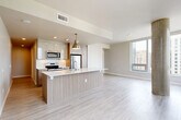 Located on the 15th floor at 846 108th Ave NE in Bellevue, WA, this 2-bedroom, 2-bathroom residence offers a modern, thoughtfully designed layout across a single floor. The open-concept kitchen and living area serves as the heart of the home, featuring a large center island with a white quartz countertop, an integrated sink, and warm wood-toned cabinetry. Stainless steel appliances, including a refrigerator, microwave, and range, complement the contemporary aesthetic, while pendant lighting adds a polished finishing touch. Light hardwood-style flooring runs throughout the main living areas, enhancing the bright, airy atmosphere. The living area benefits from floor-to-ceiling windows and a distinctive exposed concrete column, framing panoramic views of the Bellevue skyline and surrounding greenery. Both bedrooms are carpeted for comfort, with the primary bedroom offering generous proportions and access to natural light. The bathrooms are finished with warm wood vanity cabinetry, white countertops, illuminated mirrors, and tiled shower/tub surrounds. Two closets provide ample storage, and a hallway connects the private and shared spaces seamlessly. The overall design is clean, neutral, and contemporary throughout.