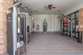 Located in Atlanta, GA, this fitness center offers a comprehensive and well-appointed exercise environment designed to meet a wide range of workout needs. The space is defined by a compelling blend of modern and industrial aesthetics, with warm exposed brick accent walls contrasting against clean white surfaces and striped multi-toned carpeted flooring with bold orange accents throughout.

The facility is organized to accommodate both cardio and strength training disciplines. A dedicated cardio zone features a row of treadmills and elliptical machines positioned near large glass-panel doors and windows, allowing ample natural light to fill the space and providing views of the adjacent common areas. Ceiling fans overhead contribute to a comfortable training atmosphere.

The strength training area is equally well-resourced, housing a multi-functional cable machine system loaded with accessories including medicine balls and resistance attachments, a full dumbbell rack with a flat bench, and a dedicated leg extension/curl machine. Barbells and weight plates are also available for free weight training.

Large floor-to-ceiling mirrors are strategically placed along the brick walls, visually expanding the space while allowing users to monitor their form. A wall-mounted television and a built-in water fountain add further convenience. Steel-framed glass partition doors connect the fitness center to neighboring amenity spaces, enhancing the open, connected feel of the overall facility.
