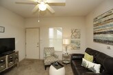 This single-floor residence offers a thoughtfully arranged open-concept layout that seamlessly connects the living, dining, and kitchen areas. The living room is a welcoming space finished with plush carpet, ceiling fans, and ample natural light streaming through window blinds. It comfortably accommodates a seating arrangement with a leather sofa, accent chair, and entertainment area, creating a relaxed and functional gathering space.

The kitchen is efficiently designed with white cabinetry, a full suite of appliances including a refrigerator, range, microwave, and dishwasher, and a breakfast bar with bar stool seating that doubles as a convenient dining counter. Adjacent to the kitchen is a dedicated dining area with room for a full dining table set.

The unit includes two bedrooms, each carpeted and equipped with ceiling fans. Both rooms offer comfortable proportions, with windows that bring in natural light. One bedroom features a walk-in closet, providing generous storage. The bathroom is accessed via a hallway and includes a vanity with a large mirror, tile flooring, and a tub-shower combination.

Throughout the unit, a textured ceiling, neutral wall tones, and consistent finishes create a cohesive and livable ambiance suited for a variety of residents.