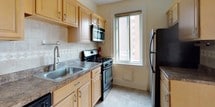 This single-floor residence combines classic architectural details with functional updates throughout its well-organized layout. The living and dining areas are distinguished by gleaming parquet wood flooring in a herringbone-style pattern, crown molding, and elegant French doors with glass panes that allow natural light to flow freely between rooms. Radiator heating units are present in multiple rooms, consistent with traditional building construction. The decorative wall paneling moldings add a refined character to the living spaces and bedrooms.

The bedrooms feature polished hardwood flooring, recessed wall paneling, crown molding, and closet access, maintaining the consistent classic aesthetic found throughout the unit. A central hallway connects the private rooms, finished with the same warm hardwood flooring and flush-mount ceiling lighting.

The kitchen is efficiently laid out with light maple cabinetry, granite-style countertops, a tile backsplash, and stainless steel appliances including a dishwasher, gas range, microwave, and refrigerator. A window provides natural light to the workspace.

The bathroom features a clean, bright design with white subway tile, a decorative mosaic tile border, a soaking tub with overhead shower, a vanity with storage, and a natural light-admitting window.
