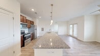 Located at 109 Capstone Way in Commerce, GA, this one-bedroom, one-bathroom residence offers a well-designed single-floor layout that maximizes its footprint with an open, airy feel. The heart of the home is the open-concept kitchen, dining, and living area, where a generously sized granite-topped island serves as a central feature. Pendant lighting hangs above the island, adding a modern touch, while rich walnut-toned cabinetry and a full suite of stainless steel appliances — including a refrigerator, range, and built-in microwave — complete the kitchen. Light wood-style flooring runs throughout the entire unit, contributing to a clean, cohesive aesthetic. The living area is bright, benefiting from a glass door that invites natural light and provides outdoor access. The bedroom is comfortably proportioned, featuring a large window with views of the surrounding greenery and access to a walk-in closet outfitted with wire shelving and organizational racks. The bathroom includes a combined tub and shower, a vanity with granite countertop matching the kitchen, and warm gold-toned fixtures. Neutral walls and consistent finishes throughout create a calm, move-in-ready atmosphere well-suited for comfortable everyday living.