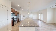 Located at 109 Capstone Way in Commerce, GA, this one-bedroom, one-bathroom residence offers a well-designed single-floor layout that maximizes its footprint with an open, airy feel. The heart of the home is the open-concept kitchen, dining, and living area, where a generously sized granite-topped island serves as a central feature. Pendant lighting hangs above the island, adding a modern touch, while rich walnut-toned cabinetry and a full suite of stainless steel appliances — including a refrigerator, range, and built-in microwave — complete the kitchen. Light wood-style flooring runs throughout the entire unit, contributing to a clean, cohesive aesthetic. The living area is bright, benefiting from a glass door that invites natural light and provides outdoor access. The bedroom is comfortably proportioned, featuring a large window with views of the surrounding greenery and access to a walk-in closet outfitted with wire shelving and organizational racks. The bathroom includes a combined tub and shower, a vanity with granite countertop matching the kitchen, and warm gold-toned fixtures. Neutral walls and consistent finishes throughout create a calm, move-in-ready atmosphere well-suited for comfortable everyday living.