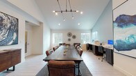 Located at 7942 Pocket Rd in Sacramento, California, this single-story space is thoughtfully designed to serve as a professional meeting and work environment. The interior is anchored by a generously sized dark wood conference table surrounded by leather upholstered chairs, accommodating a full team comfortably. Vaulted ceilings soar overhead, creating an airy, open atmosphere that enhances the sense of scale throughout the main area. An industrial-style multi-arm chandelier provides a stylish focal point while delivering ample ambient lighting above the conference table, complemented by recessed ceiling fixtures.

Natural light streams in through multiple windows fitted with white blinds, offering views of the surrounding outdoor greenery. A dedicated workstation area lines one wall, equipped with dark cabinetry, ergonomic seating, and computer equipment, providing a functional workspace alongside the collaborative meeting setup. A comfortable lounge corner features upholstered accent chairs ideal for informal discussions.

The space is distinguished by striking large-scale abstract artwork in deep blues and teals displayed prominently on the walls, alongside a reclaimed wood accent wall that introduces organic texture and warmth. Light-toned tile flooring runs throughout, tying the clean, contemporary aesthetic together cohesively.