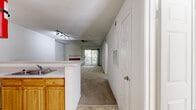 This two-bedroom, one-bathroom unit in Columbia, MD is laid out on a single floor with a practical, open-concept design. The living room serves as the focal point of the space, featuring vaulted ceilings, a ceiling fan, and a brick-surround fireplace. A sliding glass door leads to a private balcony with a white-railed deck and leafy outdoor views, allowing natural light to fill the room. Neutral carpet runs throughout the living and bedroom areas, creating a cohesive feel.

The kitchen is open to the main living area and separated by a peninsula breakfast bar with a light countertop surface. Warm-toned wood cabinetry lines the walls in a U-shaped configuration, accompanied by white appliances including a range, dishwasher, and refrigerator. Track lighting illuminates both the kitchen and the adjacent dining or flex space.

Both bedrooms are carpeted and feature neutral walls. One bedroom includes a sliding glass door opening to the balcony, while the other offers a large window with outdoor views. The full bathroom is finished with tile flooring, a white vanity with storage, a large mirror, and a tub-shower combination.