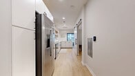 Located at 5395 Martway St in Mission, KS, this thoughtfully designed one-bedroom, one-bathroom unit offers a clean, modern aesthetic across a single floor. Light hardwood flooring runs throughout, unifying the space and enhancing the bright, airy atmosphere created by a crisp white color palette.

The kitchen is a standout feature, equipped with stainless steel appliances including a French door refrigerator, electric range, built-in microwave, and dishwasher. White flat-front cabinetry is complemented by open natural wood shelving and a subway tile backsplash, while white quartz countertops provide ample workspace. A window at the end of the kitchen draws in natural light.

A sleek sliding barn door with matte black hardware provides a stylish transition into the bedroom, which is a cozy, well-proportioned retreat with neutral walls and continued hardwood flooring. The space accommodates a queen bed comfortably.

The bathroom maintains the home's clean design language with light wood-look tile flooring, a white vanity, and a full tub-shower combination finished in white tile. The overall ambiance of the unit is modern and minimalist, with consistent use of black hardware accents and natural wood tones adding warmth throughout.