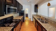 Located in Charlotte's 28277 zip code, this single-story residence offers a thoughtfully designed layout with distinct living, sleeping, and kitchen areas. The galley-style kitchen is a standout feature, showcasing rich dark espresso cabinetry, granite countertops, a subway tile backsplash, and stainless steel appliances including a built-in microwave. Warm hardwood-style flooring runs throughout the kitchen, and a decorative arched pass-through with pendant lighting connects it seamlessly to the living area, adding an architectural detail that enhances the open feel.

The living room is generously sized, filled with natural light through large windows with views of surrounding greenery, and finished with plush neutral carpet and crown molding. A ceiling fan with light fixture is featured in one of the carpeted bedrooms, which also benefits from a bright window. Another bedroom includes built-in shelving and direct access to a full bathroom. The bathroom features a single-sink vanity with dark cabinetry, a wide mirror, and a tub-shower combination, all set on hardwood-style flooring. Clean white walls and neutral tones throughout lend the space a bright, welcoming ambiance.
