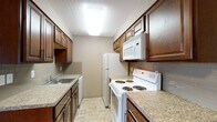 Located at 203 East Sharpe Avenue in Spokane, Washington, Unit 204 is a thoughtfully designed single-floor residence that balances functionality with comfortable living. The galley-style kitchen is a standout feature, outfitted with rich dark-wood cabinetry, granite-look countertops, a tiled backsplash, and white appliances including a range, over-the-range microwave, dishwasher, and refrigerator. Tile flooring runs throughout the kitchen, which transitions seamlessly into the open living area. The living space is carpeted and receives natural light through windows that offer views of the surrounding neighborhood, with a wall-mounted air conditioning unit providing climate control. Baseboard heating is present throughout the unit. The bedroom is generously sized with plush carpeting, a window for natural light, and a dedicated closet with double doors and a full-length hanging rod. The bathroom features tile flooring, a full tub-shower combination with a white surround, a toilet, and a dark-wood vanity with an undermount sink and dark countertop. The unit's neutral warm-toned walls and textured ceilings create a cozy, understated ambiance throughout.