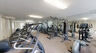 Located at 4573 Whisper Lake Dr in Black Jack, Missouri, this fitness center offers a compact yet thoroughly equipped workout facility on a single floor. The space is designed to maximize functionality, with floor-to-ceiling mirrors lining the walls to create an expansive, open feel and allow users to monitor their form throughout their workouts.

The cardio section features multiple treadmills and elliptical trainers, providing ample options for aerobic exercise. The strength training area is equally well-appointed, housing a variety of cable machines, lat pulldown stations, chest press rigs, and adjustable benches — offering a comprehensive range of resistance-based workout options. Additional stationary bikes round out the cardio equipment selection.

Neutral-toned carpet covers the floor throughout, providing cushioning underfoot and a clean, polished appearance. Recessed fluorescent lighting ensures the space is brightly and evenly illuminated. The white walls and mirrored surfaces work together to amplify the sense of space, making the gym feel larger than its footprint suggests. Ventilation is provided through ceiling vents, maintaining a comfortable environment during exercise. Overall, this fitness center is a well-organized and fully functional facility suited for a broad range of fitness routines.