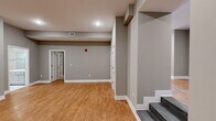This single-floor residence offers a thoughtfully organized layout encompassing three bedrooms, three bathrooms, a kitchen, living room, hallway, and dedicated closet space. Warm-toned hardwood-style flooring runs consistently throughout the main living areas and bedrooms, complemented by neutral gray walls and crisp white trim, creating a cohesive and clean aesthetic.

The open living area is generously proportioned, featuring recessed lighting and straightforward access to adjacent rooms via a connecting hallway. A staircase entry element adds architectural dimension to the space. The kitchen is equipped with stainless steel appliances, including a range, over-the-range microwave, and side-by-side refrigerator, paired with white shaker-style cabinetry extending to the ceiling for ample storage and gray countertops.

The primary bedroom provides comfortable space with a ceiling fan and an open closet alcove with shelving. A dedicated walk-in closet with dual hanging rods and shelving adds practical storage. The bathrooms are finished with white subway tile featuring a blue mosaic accent border, marble-look tile flooring, white vanities, and brushed nickel fixtures. One bathroom includes a soaking tub, while another features a glass-enclosed walk-in shower.