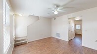 This two-story townhouse in New Orleans, Louisiana offers a well-designed layout across three bedrooms and two and a half bathrooms. The main living area features warm wood-look flooring, neutral white walls, and a ceiling fan, creating a bright and comfortable space. A staircase leads to the upper level, where carpeted bedrooms provide a quiet retreat, each equipped with ceiling fans and ample natural light from windows with blinds. The primary bedroom includes access to a full bathroom fitted with a framed glass-door shower stall and a wood-toned vanity. A convenient half bathroom on the main floor features the same wood-look flooring and a matching wood-cabinet vanity. The kitchen is a functional highlight, outfitted with warm honey-toned cabinetry, dark countertops, a central island for additional prep and dining space, white appliances including a dishwasher and range, and multiple windows that fill the room with natural light. A dedicated laundry room houses a full-size washer and dryer alongside built-in shelving for added storage. The townhouse also benefits from a central HVAC system and ceiling fans in every room, ensuring year-round comfort throughout this practical and well-appointed New Orleans home.