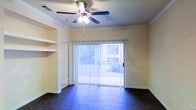 This single-floor residence offers a clean, functional layout with thoughtful design details throughout. The living area serves as the heart of the space, showcasing rich dark hardwood flooring that grounds the room with warmth and contrast against the light-toned walls. Crown molding lines the ceiling, adding a refined architectural touch, while a ceiling fan with integrated lighting provides both comfort and practicality overhead. Built-in shelving flanks the entryway, offering convenient storage and display space that contributes to the room's organized character. A large sliding glass door dominates one wall of the living area, dressed with vertical blinds that allow for adjustable light control. The door opens to an outdoor area, inviting natural light deep into the interior and offering a view of the surrounding exterior. The overall ambiance is bright and airy, with a neutral color palette that creates a versatile backdrop. The single-floor layout ensures ease of movement throughout the space, making it an accessible and practical living environment. Every element — from the flooring to the architectural trim — works together to deliver a cohesive, well-appointed interior.