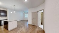 This single-story residence features a cohesive design throughout, with warm wood-style flooring extending across the living areas and bedrooms. The open-concept kitchen is a standout, showcasing dark espresso cabinetry reaching toward the ceiling, granite countertops, a central island with additional granite surface space, stainless steel appliances including a refrigerator, range, microwave, and dishwasher, and pendant lighting overhead. The kitchen flows naturally into the main living area, which benefits from natural light through window treatments and is equipped with a ceiling fan.

The bedrooms are generously sized, each with wood-style flooring, ceiling fans, and access to natural light via windows with blinds. One bedroom includes a private en-suite bathroom and direct access to an additional room or hallway. A walk-in closet with wire shelving provides ample storage. The bathroom features a granite-topped dark vanity, tile flooring, and a tub-shower combination. A dedicated laundry area accommodates a full-size washer and dryer side by side, adding everyday convenience. The overall palette of white walls, warm flooring, and dark cabinetry creates a clean, modern aesthetic throughout.