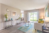 Located at 236 Queens Ct in Chesapeake, Virginia, this single-story residence offers a thoughtfully arranged floor plan designed for comfortable everyday living. The open living area is anchored by durable wood-style flooring, neutral-toned walls, and a textured ceiling. A large sliding glass door floods the space with natural light and provides views of the outdoors, creating an airy, welcoming atmosphere that flows seamlessly into a dedicated dining area, which features a classic chandelier and a window overlooking the exterior.

The galley-style kitchen is efficiently designed with rich dark wood cabinetry, light-toned countertops, a double sink, and white appliances including a range and refrigerator. Wood-style flooring continues throughout, adding cohesion to the layout.

The residence includes multiple bedrooms, each carpeted for comfort. The primary bedroom features a walk-in closet, while a secondary bedroom showcases a bright yellow accent wall and a window with outdoor views. Both rooms offer ample space for furnishings. The bathroom includes a full soaking tub with a shower combination and clean white fixtures. Throughout, the home maintains a consistent, neutral palette complemented by warm lighting.