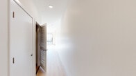 This well-appointed one-bedroom, one-bathroom unit offers a thoughtfully designed layout across a single floor. Light wood flooring runs continuously throughout the space, creating a cohesive and airy feel.

The combined kitchen and living area forms the heart of the unit. The kitchen is outfitted with light wood cabinetry, a white subway tile backsplash, stainless steel appliances including a refrigerator, range, microwave, and dishwasher, and a sleek countertop with an undermount sink. A black track lighting system overhead provides ample illumination. The open living area is bathed in natural light from a dramatic bank of large, grid-paned windows that offer expansive city skyline views, with a wall-mounted mini-split climate control unit also present.

The bedroom is a calm, neutral space featuring a ceiling fan with integrated lighting and direct access to a dedicated closet with built-in double shelving. A bright hallway connects the living spaces to the private areas, lined with recessed lighting and louvered closet doors for additional storage.

The bathroom is clean and modern, featuring a wood-toned vanity with a white countertop, a full tub and shower combination surrounded by white grid tile, and light wood flooring to match the rest of the unit.