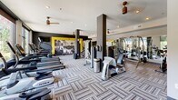 The Anderson Flats Athletic Club at 2841 Manorcrest Ct in Raleigh, NC is a thoughtfully designed fitness center offering a comprehensive workout experience within a single, open-plan floor. The space is outfitted with a full suite of TRUE-brand equipment, including treadmills, ellipticals, stair climbers, and a broad selection of strength and resistance machines, providing members with everything needed for a complete workout routine.

The interior design blends contemporary aesthetics with motivational energy. Bold black and yellow accent walls feature large-format athletic photography and Anderson Flats branding, lending the space a dynamic, gym-club atmosphere. Dark structural columns add architectural definition and help organize distinct workout zones without disrupting the open feel of the room. Patterned tile-effect carpeting covers the floor throughout, providing both comfort and visual interest.

Natural light is a standout feature, with floor-to-ceiling windows along one wall offering expansive views of the outdoor pool area and lush landscaping beyond. This connection to the outdoors creates an uplifting environment for exercise. Ceiling fans are distributed throughout to maintain comfortable airflow, complemented by recessed lighting. A built-in shelving unit and small cabinetry area provide additional utility. The overall ambiance is modern, energetic, and well-maintained — a premium amenity space designed to support an active lifestyle.