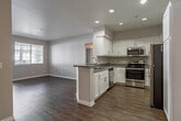 Located at 8250 Vineyard Ave in Rancho Cucamonga, CA, this single-floor residence offers a thoughtfully designed layout with a clean, contemporary aesthetic throughout. The open-concept living area features warm hardwood-style flooring and crisp white walls, creating a bright and airy atmosphere. Recessed lighting illuminates the space, which flows seamlessly into a well-appointed kitchen outfitted with white cabinetry, granite-style countertops, a breakfast bar, and a full suite of stainless steel appliances including a refrigerator, range, and over-the-range microwave. The bedrooms are finished with rich, darker-toned hardwood-style flooring and are filled with natural light from large windows fitted with blinds. One bedroom features a ceiling fan and another includes mirrored sliding closet doors, enhancing both function and the sense of space. The attached garage offers a spacious, clean concrete floor and an automatic opener, with additional space accommodating a washer. A covered outdoor patio extends the living space to the exterior, overlooking a landscaped community setting with mature trees and manicured hedges — ideal for relaxing in the Southern California climate.
