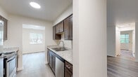 Located at 581 Lake Forest Dr in Norton Shores, Michigan, this three-bedroom, one-bathroom single-floor home offers a practical and well-appointed layout. The galley-style kitchen is a standout feature, equipped with rich dark-stained cabinetry, light granite-style countertops, a stainless steel sink, dishwasher, and black electric range with over-the-range microwave. Wood-style luxury vinyl plank flooring runs throughout the main living areas, lending a clean, contemporary feel. The living room is bright and open, benefiting from natural light and sliding glass door access to a private balcony with outdoor views — ideal for everyday relaxation. Hallways connect the living spaces to the bedroom wing, where plush carpeting adds comfort underfoot. The primary bedroom is generously sized and features a mirrored sliding-door closet and a window overlooking lush greenery. Additional bedrooms include closet storage. The full bathroom is clean and functional, featuring a tiled tub-shower combination. Carpeted closets throughout the home provide ample storage. The overall aesthetic is neutral and move-in ready, with cream-toned walls and consistent finishes creating a cohesive, welcoming atmosphere throughout.