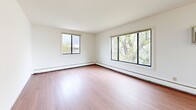 This two-bedroom, one-bathroom single-floor unit in Monona, Wisconsin offers a bright and functional layout with a clean, neutral aesthetic throughout. The living room is a standout space, featuring warm hardwood-style flooring, large windows on multiple walls, and sweeping views of a nearby lake framed by lush greenery — an exceptional natural backdrop that fills the room with abundant natural light. A ceiling fan and wall-mounted air conditioning unit ensure year-round comfort. The galley-style kitchen is efficiently designed with warm oak cabinetry, ample upper and lower storage, a double-basin sink, and white appliances including a range, microwave, and refrigerator. Hardwood-style flooring continues through the kitchen, which connects conveniently to the rest of the unit. Both bedrooms are carpeted for comfort and feature louvered bi-fold closet doors providing generous storage space. The primary bedroom is a well-proportioned retreat with a window offering peaceful water views. The full bathroom includes a wide vanity with under-sink cabinetry, a large mirror with overhead lighting, and tile flooring. Baseboard heating is present throughout, and the overall layout is practical and well-connected, making efficient use of the available space.