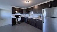 This contemporary apartment showcases a harmonious blend of style and functionality. The heart of the home is the modern kitchen, featuring rich, dark wood cabinetry contrasting beautifully with white countertops and a subway tile backsplash. Stainless steel appliances, including a range, dishwasher, and refrigerator, complete the culinary space.

The living area is bathed in natural light, courtesy of large windows that offer picturesque views. Ceiling fans and window-mounted air conditioning units ensure comfort throughout the seasons. The space boasts a mix of flooring, with sleek tile in the kitchen and bathroom, and plush carpeting in the living and bedroom areas.

The bathroom is tastefully appointed with a single vanity, large mirror, and a shower/tub combination. White tiles and neutral tones create a clean, spa-like atmosphere. Throughout the apartment, recessed lighting and modern fixtures provide ample illumination.

The open floor plan allows for easy flow between rooms, making the space feel larger and more connected. Built-in closets offer practical storage solutions. The overall design aesthetic is minimalist and contemporary, with a neutral color palette that allows for personal touches in decor. This well-designed apartment offers a perfect balance of comfort and modern living.
