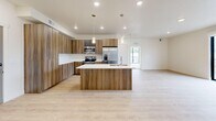 Located at 6151 Van Winkle in Holladay, Utah, this thoughtfully designed one-bedroom, one-bathroom unit offers a clean, contemporary aesthetic throughout. The open-concept kitchen and living area serves as the heart of the space, featuring striking wood-grain cabinetry that extends floor to ceiling, a large central island with a white quartz countertop and undermount sink, stainless steel appliances including a refrigerator, range, and microwave, and pendant lighting that adds a warm, modern touch. Light hardwood flooring runs throughout the main living areas, enhancing the bright and airy atmosphere. The living area connects seamlessly to a private balcony through large sliding glass doors, framing impressive views of the surrounding Wasatch Mountains. The spacious bedroom is finished with plush carpet, oversized windows, and its own sliding door access to the balcony, filling the room with abundant natural light and mountain scenery. The full bathroom is finished with the same wood-grain cabinetry, a white countertop vanity, and a tub-shower combination, maintaining a consistent modern palette. Clean white walls and recessed lighting throughout contribute to the unit's crisp, contemporary feel.