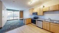 Located at 601 SE Main St in Minneapolis, MN, this two-bedroom, one-bathroom unit offers a practical and well-organized layout across a single floor. The open-concept kitchen, dining, and living area serves as the heart of the home, featuring light maple cabinetry, granite-style countertops, a peninsula breakfast bar, and a full suite of stainless steel appliances including a refrigerator, electric range, dishwasher, and microwave. Light hardwood-style flooring flows through the kitchen, transitioning to patterned tile-cut carpeting in the living and bedroom areas, adding texture and warmth throughout. Both bedrooms are comfortably sized, with large windows that invite natural light and provide views of the surrounding neighborhood. An exposed cylindrical duct runs through the bedrooms, lending an industrial character to the space. The unit includes four closets, offering generous storage options. The bathroom is finished in clean white tile with accessible grab bars and a combined tub and shower. The unit also features a keypad-secured entry door. With its functional design, ample storage, and modern finishes, this unit is well-suited for everyday living in the heart of Minneapolis.