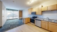 Located at 601 SE Main St in Minneapolis, MN, this two-bedroom, one-bathroom unit offers a practical and well-organized layout across a single floor. The open-concept kitchen, dining, and living area serves as the heart of the home, featuring light maple cabinetry, granite-style countertops, a peninsula breakfast bar, and a full suite of stainless steel appliances including a refrigerator, electric range, dishwasher, and microwave. Light hardwood-style flooring flows through the kitchen, transitioning to patterned tile-cut carpeting in the living and bedroom areas, adding texture and warmth throughout. Both bedrooms are comfortably sized, with large windows that invite natural light and provide views of the surrounding neighborhood. An exposed cylindrical duct runs through the bedrooms, lending an industrial character to the space. The unit includes four closets, offering generous storage options. The bathroom is finished in clean white tile with accessible grab bars and a combined tub and shower. The unit also features a keypad-secured entry door. With its functional design, ample storage, and modern finishes, this unit is well-suited for everyday living in the heart of Minneapolis.