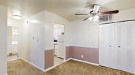 This single-floor residence offers a practical and comfortable layout across several well-defined living areas. The main living space features warm beige carpet underfoot and a ceiling fan with integrated lighting overhead. A distinctive two-tone wall treatment — white upper walls paired with a dusty rose lower half divided by white chair rail molding — adds a touch of character to the space. A louvered closet door provides convenient built-in storage, while a passthrough opening leads directly into the kitchen.

The kitchen is well-appointed with white cabinetry offering ample storage, granite-style countertops, a double stainless steel sink, and a warm earth-toned tile backsplash. White appliances including a refrigerator and range complete the functional cooking space, with light wood-look flooring tying the area together.

The bedrooms are carpeted and bright, each featuring ceiling fans and windows with blinds that invite natural light while maintaining privacy. The rooms offer generous wall space suitable for a variety of furniture arrangements.

The bathroom is finished with earth-toned tile flooring, a white vanity with an integrated sink, and a full tub-shower combination enclosed by white square wall tile and a classic chrome rod and curtain setup, creating a clean and timeless look throughout.