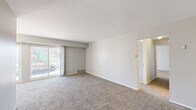 This single-floor, 2-bedroom, 1-bathroom residence offers a practical and comfortable layout across a modest but efficiently organized footprint. The living area serves as the central gathering space, finished with wall-to-wall carpet and neutral gray-toned walls. A full-width sliding glass door fills the room with natural light and provides direct access to an outdoor area, offering views of surrounding trees and greenery.

The galley-style kitchen is situated adjacent to the living area and features light wood cabinetry lining both walls, dark countertops, tile flooring, and white appliances including a range and refrigerator. Ample upper and lower cabinet storage maximizes the use of the space.

The spacious primary bedroom includes a large sliding-door closet and connects directly to a dedicated closet area and the full bathroom. The bathroom is finished with white square tile surrounding a shower-tub combination and includes a vanity with wood cabinetry. The second bedroom is bright, with a large window dressed with vertical blinds, carpeted floors, and clean white walls. A hallway connects all rooms, contributing to the home's efficient and cohesive flow.