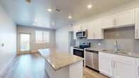 Located at 8771 Jordan Valley Way in West Jordan, Utah, this thoughtfully designed 2-bedroom, 3-bathroom unit offers a clean, modern aesthetic across a well-organized single-floor layout. The kitchen serves as a central highlight, featuring crisp white shaker cabinetry, granite countertops, a subway tile backsplash, a central island with additional counter space, and a full suite of stainless steel appliances including a range, microwave, dishwasher, and refrigerator. Wood-look luxury vinyl flooring flows throughout the kitchen and living areas, providing a warm, durable foundation. Both bedrooms are carpeted in plush, neutral-toned carpet and are served by ceiling fans with natural light from window blinds. The spacious primary bedroom includes its own dedicated walk-in closet with wire shelving systems, and a second closet provides additional storage. The bathrooms are finished with granite-topped white vanities, wood-look flooring, and tiled surrounds. One bathroom features a private water closet for added privacy. A connecting hallway ties the layout together efficiently. The unit presents a fresh, move-in-ready interior with consistent finishes throughout.