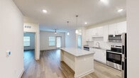 Located at 125 New Hanover St in Beaufort, SC, this well-appointed single-story residence offers a thoughtfully designed open-concept layout with two bedrooms and two bathrooms. The combined kitchen and living area serves as the heart of the home, anchored by a granite-topped center island with pendant lighting overhead. The kitchen is outfitted with crisp white cabinetry, a tiled backsplash, stainless steel appliances including a refrigerator, range, microwave, and dishwasher, and a double basin sink. Recessed lighting and light hardwood-style flooring run throughout, creating a clean, cohesive aesthetic. The living area is generously sized, featuring a ceiling fan, natural light from multiple windows, and a glass-panel door that opens to the exterior. Both bedrooms are bright and well-proportioned, each equipped with ceiling fans and windows with blinds. The primary bedroom features its own en suite bathroom, complete with a granite vanity, glass-enclosed shower, and a dedicated walk-in closet with wire shelving. A second full bathroom serves the additional bedroom. A dedicated laundry room houses a full-size Whirlpool washer and dryer with wire shelving above. Two closets provide ample storage throughout the residence.