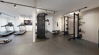 This modern fitness facility at 2165 Benvoulin Crt in Kelowna, BC, is designed to support a full range of workout routines within a generously sized, single-floor space. The interior features a clean, contemporary aesthetic with white walls, light-toned structural columns, and durable rubber flooring throughout — a practical and professional choice for a high-traffic fitness environment. Track lighting runs across the ceilings, providing bright, even illumination across all workout zones.

The strength training area is comprehensively outfitted, featuring a full rack of kettlebells and dumbbells, adjustable benches, a cable machine, a power rack with barbell and weight plates, and a medicine ball storage tower. Floor-to-ceiling mirrors line one wall, amplifying the sense of space and allowing users to monitor their form. A dedicated cardio zone houses multiple Spirit treadmills and an elliptical trainer, positioned near large windows fitted with roller blinds that allow natural light to filter in. A wall-mounted flat-screen display is also present in the cardio area.

The layout is thoughtfully zoned, with distinct areas for free weights, machines, and cardio, ensuring efficient use of the floor space. Ceiling-mounted HVAC units maintain comfortable airflow throughout. The overall ambiance is bright, clean, and functional — a well-appointed facility suited for diverse fitness needs.