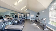 Located at 400 Haslet St in Dover, Delaware, this dedicated fitness center offers a well-equipped exercise space designed to support a full range of workout routines. The room is defined by striking vaulted ceilings that lend an open, airy feel, while soft blue-gray walls create a calm and focused atmosphere throughout. Durable rubber flooring covers the entire exercise area, providing both safety and comfort underfoot.

Natural light pours in through elegant arched windows and a set of French doors, which also offer direct access to the outdoors. Multiple wall-mounted flat-screen televisions are positioned throughout the space for entertainment during workouts. Overhead fluorescent lighting supplements the natural light, ensuring the room remains bright at all times.

The fitness center is well-stocked with a diverse selection of equipment, including multiple treadmills, stationary bikes, a cable weight machine, a rowing machine, a dumbbell rack with a full range of free weights, adjustable benches, and a step platform. A wall-mounted mirror on one end enhances the sense of space and supports form-checking during exercise. Informational charts and posted workout guides are displayed on the walls. The space is completed with a small wooden storage unit and convenient wall-mounted amenities, making it a fully functional and inviting fitness facility.