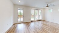 This well-designed two-story home offers a thoughtful layout across two floors, combining modern finishes with functional living spaces. The ground floor features an open-concept kitchen and living area, where light wood-look flooring flows seamlessly throughout. The kitchen is a standout, equipped with stainless steel appliances, a central island with a sink and pendant lighting, a mix of white and warm-toned cabinetry, and open shelving for added character. The living area is bright and airy, with large windows and a glass-paned door that invite abundant natural light and provide views of the outdoors. A hallway with recessed lighting and clean white walls leads to additional spaces, including an attached garage with an automatic door opener. Upstairs, the more expansive floor houses both bedrooms, each featuring plush carpeting, ceiling fans, and multiple windows that frame green outdoor views. The generously sized primary bedroom includes a walk-in closet outfitted with built-in shelving and double hanging rods. The two bathrooms are finished with neutral tile flooring, white cabinetry, quartz-style countertops, and a tiled soaking tub. Throughout the home, a consistent palette of whites and warm neutrals creates a clean, contemporary ambiance.
