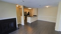 This single-floor residence offers a thoughtfully designed open-concept layout that seamlessly connects the living and kitchen areas. Dark hardwood flooring runs throughout, providing a warm, rich contrast to the neutral beige walls and white trim. The living area features a classic fireplace with a simple mantle, adding a cozy focal point to the space. A textured ceiling adds subtle architectural interest overhead, while flush-mounted lighting ensures the space is well-lit throughout.

The kitchen is a standout feature, equipped with stainless steel appliances including a refrigerator, gas range, and microwave. White cabinetry offers ample storage, while dark countertops along the peninsula provide both workspace and a casual dining or gathering spot. The peninsula also features an integrated sink, combining style with practicality. The kitchen flows naturally into the living space, making the layout ideal for entertaining.

A recessed nook in the wall near the entryway adds a charming architectural detail, offering a display or storage opportunity. Ceiling vents are positioned throughout for efficient climate control. Overall, the space presents a clean, modern aesthetic with functional design choices that balance comfort and practicality.