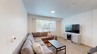 Located at 505 S Fifth St, Unit 205 in Champaign, IL, this well-appointed 4-bedroom, 4-bathroom unit offers a thoughtfully designed single-floor layout. The open-concept living room is a standout space, featuring a decorative geometric accent wall, light hardwood flooring, and large windows with horizontal blinds that invite natural light. A spacious sectional sofa and built-in media console with a beverage fridge make it an ideal gathering area.

The kitchen is outfitted with shaker-style cabinetry in a light gray finish, white quartz countertops, a classic subway tile backsplash, and stainless steel appliances including a refrigerator, range, and over-the-range microwave. A peninsula provides additional counter space and separates the kitchen from the living area.

Each of the four bedrooms features hardwood flooring and clean white walls. Several rooms include ceiling fans, windows with outdoor views, and built-in shelving. The bedrooms are compact yet functional, offering practical space for sleeping and studying.

The four bathrooms are finished with light wood-look flooring, white walls, and matte black hardware and fixtures. Each includes a glass-enclosed walk-in shower, a vanity with storage, and a toilet. A connecting hallway ties the layout together efficiently, providing easy access to all rooms throughout the unit.