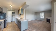 This single-floor residence is designed with a practical, open layout that connects the kitchen and living areas seamlessly. The kitchen is a standout feature, offering a galley-style configuration with gray cabinetry, light countertops, black appliances including an electric range and refrigerator, track lighting, and wood-look flooring. A peninsula counter extends toward the living area, creating a natural dividing point while maintaining an open feel. Conveniently tucked nearby is an in-unit washer, adding everyday practicality. The living room is generously sized, carpeted, and filled with natural light from multiple windows fitted with blinds. A tile-surround corner fireplace serves as a focal point, adding warmth and character to the space. A door provides access to an outdoor area. The bedroom is carpeted, well-proportioned, and includes a sliding-door closet with built-in shelving, along with a window that brings in natural light. The bathroom features a full soaking tub with a clean white surround and chrome fixtures. Throughout, neutral gray walls and consistent finishes create a cohesive, understated aesthetic.