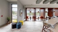 Located at 1989 Cheshire Bridge Rd NE in Atlanta's dynamic Cheshire Bridge neighborhood, this single-floor community space makes a striking first impression with its bold teal accent walls, large-format marble-look tile flooring, and an open, flowing layout that connects multiple functional zones seamlessly.

The main corridor draws visitors through vivid teal archways, with a reception-style counter near the entrance offering a welcoming workstation. A dramatic red sheer curtain acts as a design focal point and soft room divider, adding warmth and visual interest against the cool teal palette.

Floor-to-ceiling windows flood the lounge and seating areas with natural light, providing open views of the surrounding greenery and streetscape. Built-in wooden banquette booths with pendant globe lighting offer intimate nooks for conversation or work, while modular hexagonal ottomans in yellow, teal, and charcoal provide flexible, casual seating throughout.

Deeper within the space, an additional lounge and gathering area features patterned carpet, eclectic wall art, and ample seating configurations suited for both individual use and group interaction. A communal table with bar-height seating creates a collaborative work or social hub.

Throughout, the design balances energetic color with clean modern architecture, creating a welcoming, multifunctional environment that is both visually engaging and highly functional.